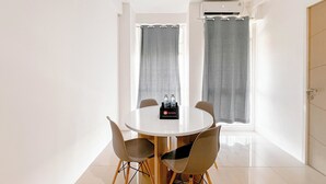 Una habitación pequeña y moderna con una mesa redonda y cuatro sillas, una ventana con cortinas y una puerta.