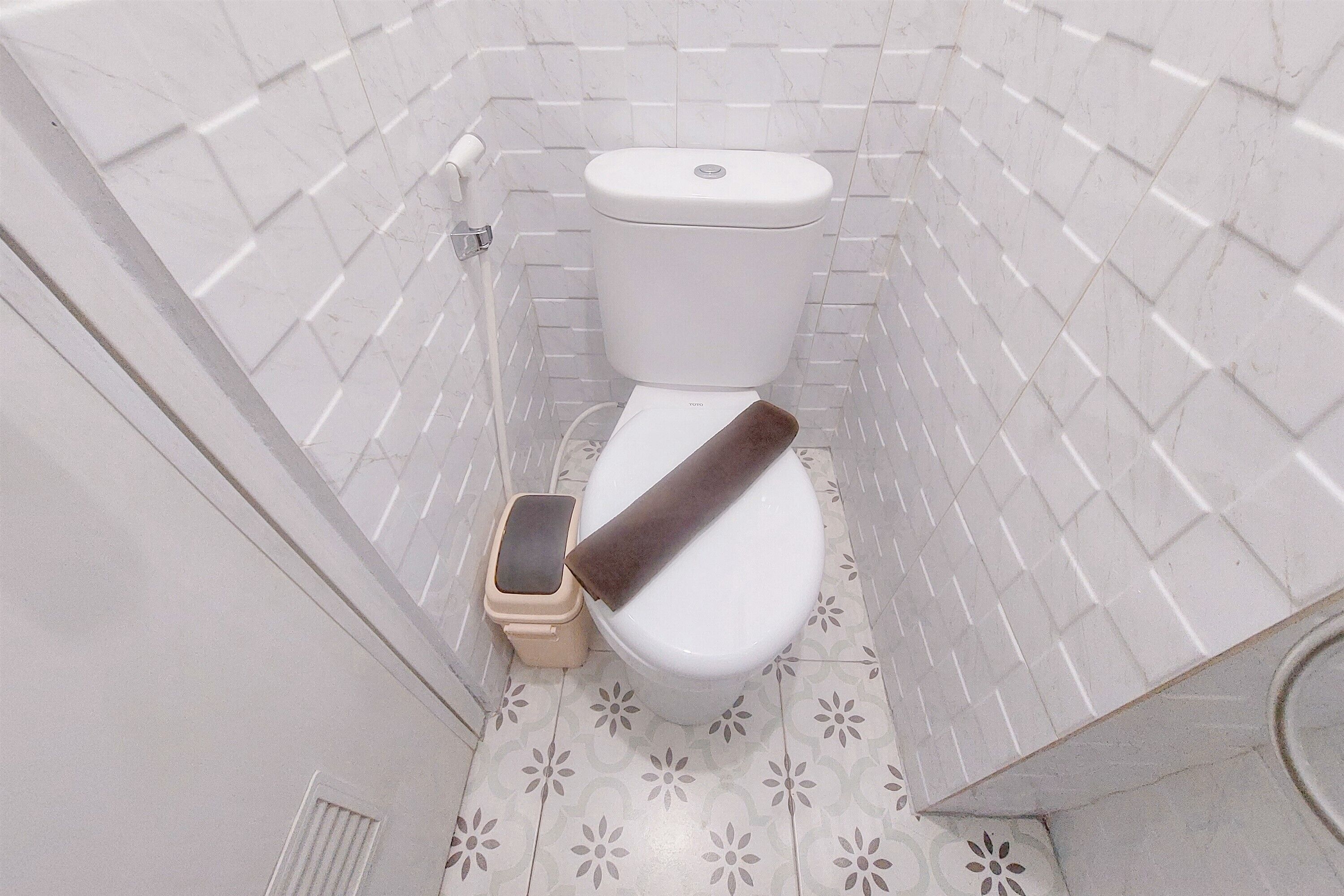 Un baño pequeño con azulejos, que incluye un inodoro, un cubo de basura y un dispensador de papel higiénico.