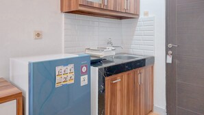 A compact kitchen with wooden cabinets, a white tiled backsplash, a black countertop, and a blue refrigerator. - Comfy And Homey Studio At Sky View Apartment (South Tangerang)
