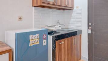 Cocina compacta con armarios de madera, salpicadero de azulejos blancos, encimera negra y refrigerador azul.