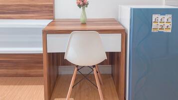 Un pequeño escritorio de madera con una silla blanca, un florero con flores y un refrigerador azul con un gráfico de mantenimiento.