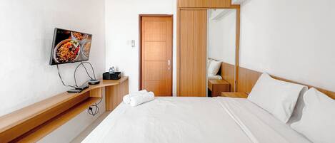 A hotel room with a bed, a TV mounted on the wall, a wooden wardrobe, and a bedside table with a lamp.