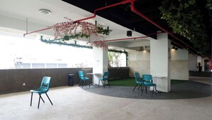 Een moderne ruimte met teal-kleuren stoelen rond een centrale tafel, een betonnen vloer, en een plafond met zichtbare leidingen en planten.