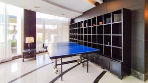 Une table de ping-pong dans une pièce dotée d’une grande fenêtre, d’une lampe et d’une étagère le long du mur.