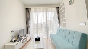 Un salon moderne avec un canapé bleu clair, un téléviseur à écran plat posé sur un meuble blanc et une table basse en verre.