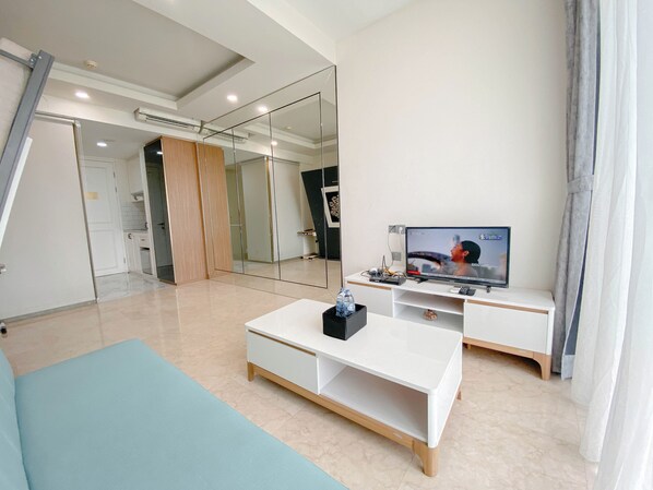 A modern living room with a flat-screen TV, a white coffee table, and a blue sofa. - Luxurious Studio At Art Deco Apartment (Bandung)