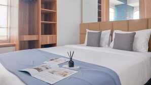 A neatly made bed with a blue bedspread, white pillows, and a magazine on the bed. There is a small vase with black candles on a white tray. - Homey 2Br Apartment At Urban Heights Residence (South Tangerang)