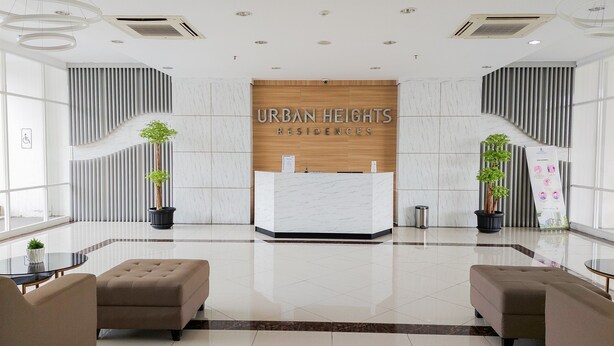 A modern reception area with a marble reception desk, two potted plants, and a sign reading "URBAN HEIGHTS RESIDENCES". - Homey 2Br Apartment At Urban Heights Residence (South Tangerang)