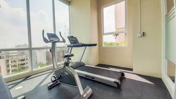 A gym with a treadmill and an elliptical machine, large windows with a view of buildings, and a small window with a plant.
