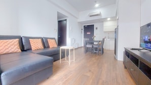 A modern living room with a sectional sofa, a small table, and a TV. - Cozy Living 2Br Apartment At Casa De Parco (Pagedangan)