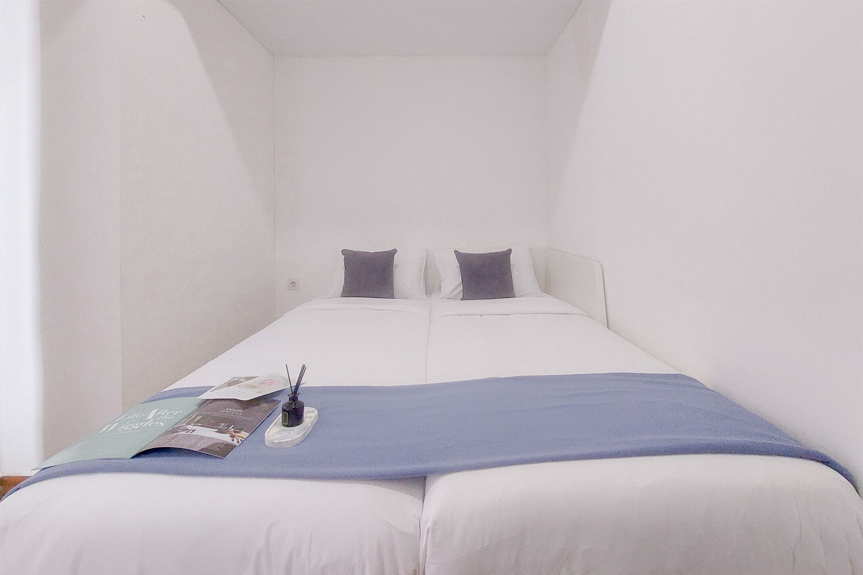 A small, white, single-bed room with a blue blanket and pillows.