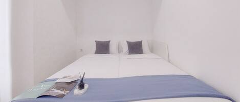 A small, white, single-bed room with a blue blanket and pillows.