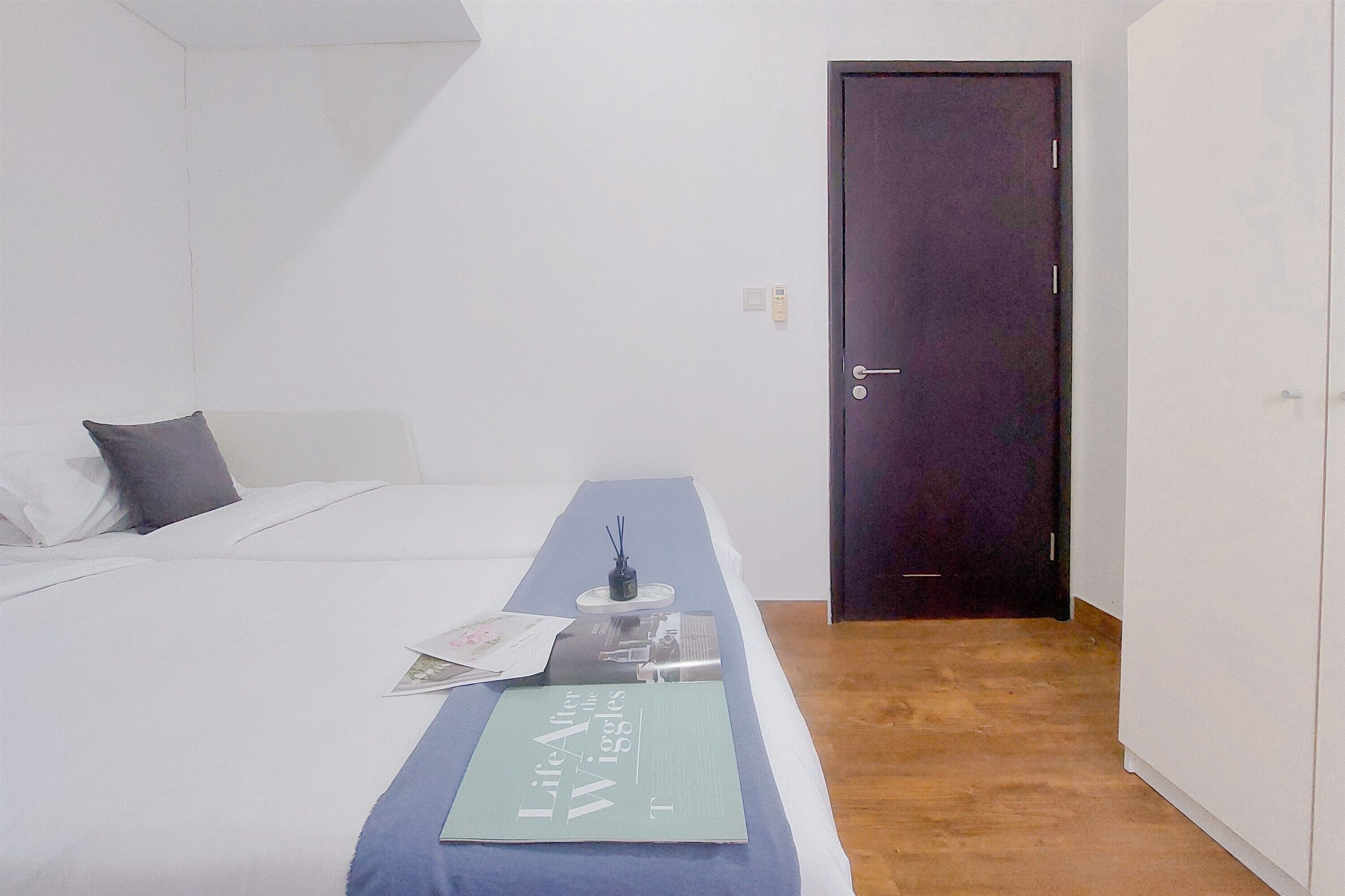 A bedroom with a bed, a bedside table with a book, a door, and a light switch on the wall.