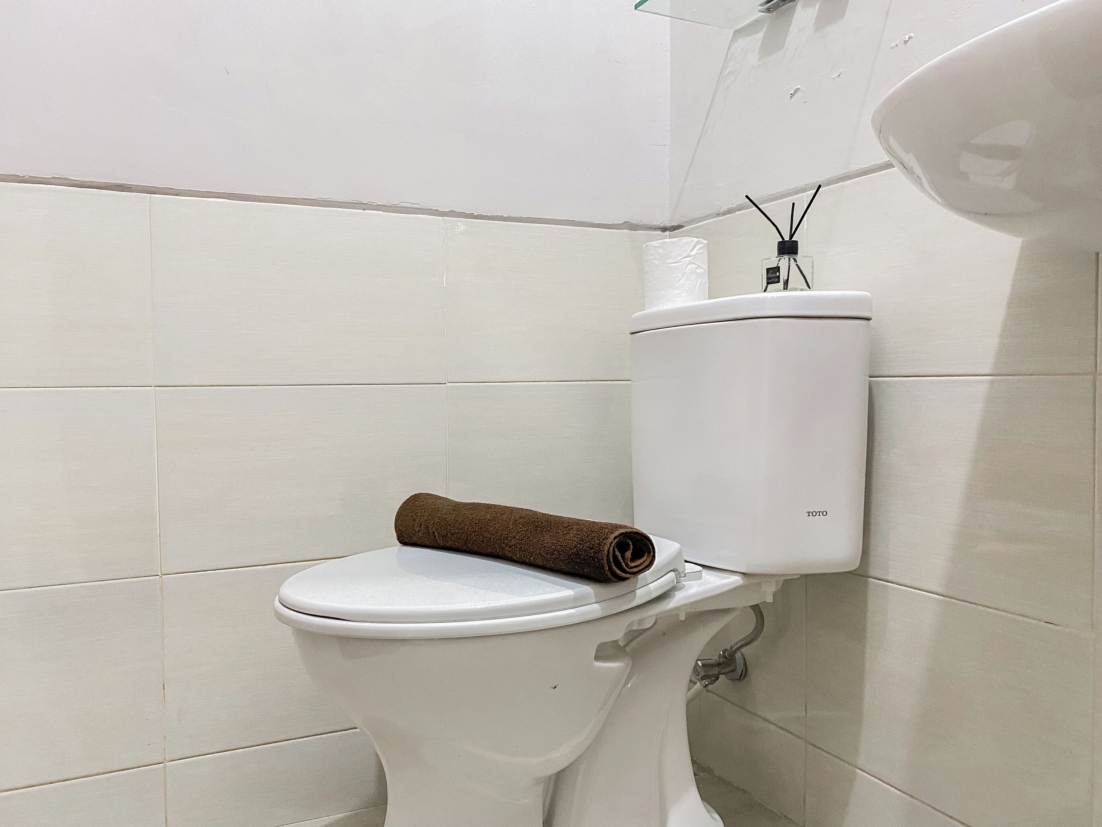 A white toilet with a brown towel on the seat, a toilet paper holder, and a bidet spray.