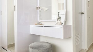 A white vanity with a mirror, a small lamp, and a framed picture of the Statue of Liberty. - Good Place And Comfortable Studio Apartment Springlake Summarecon Bekasi (Bekasi)