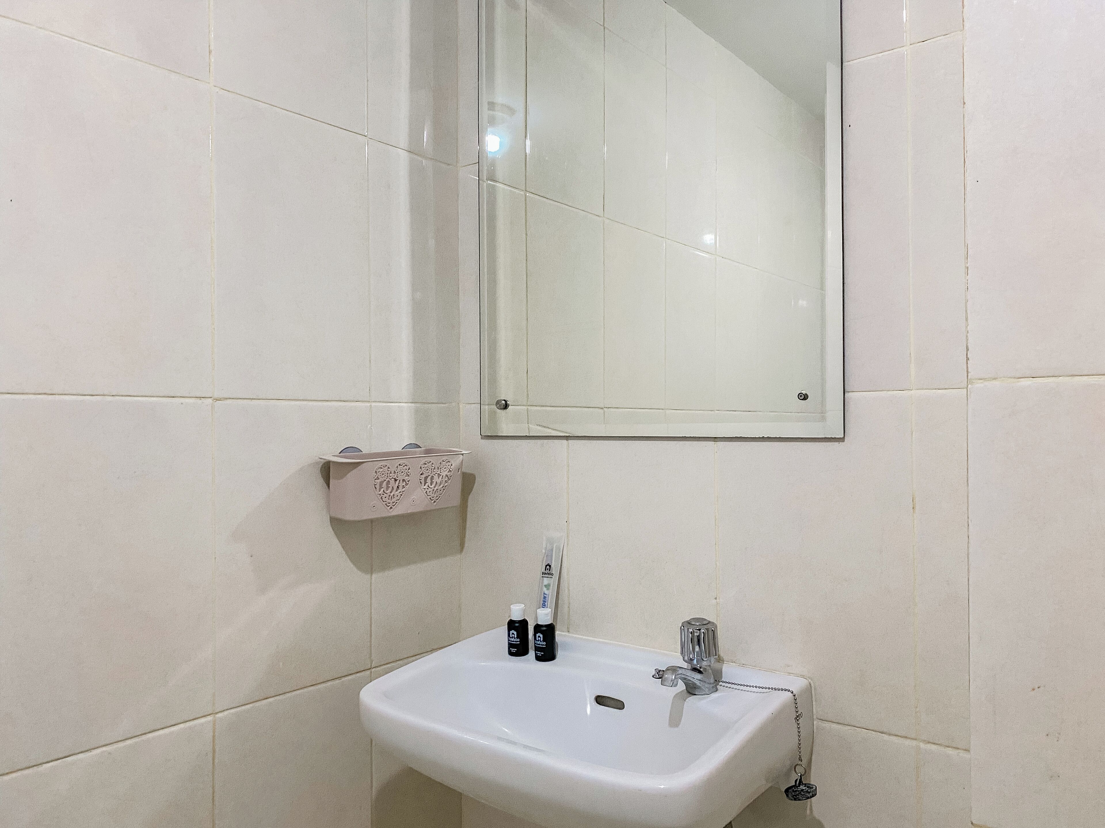 Une salle de bain avec un lavabo blanc, un miroir et un porte-serviettes doté d’un support à serviettes en forme de cœur.