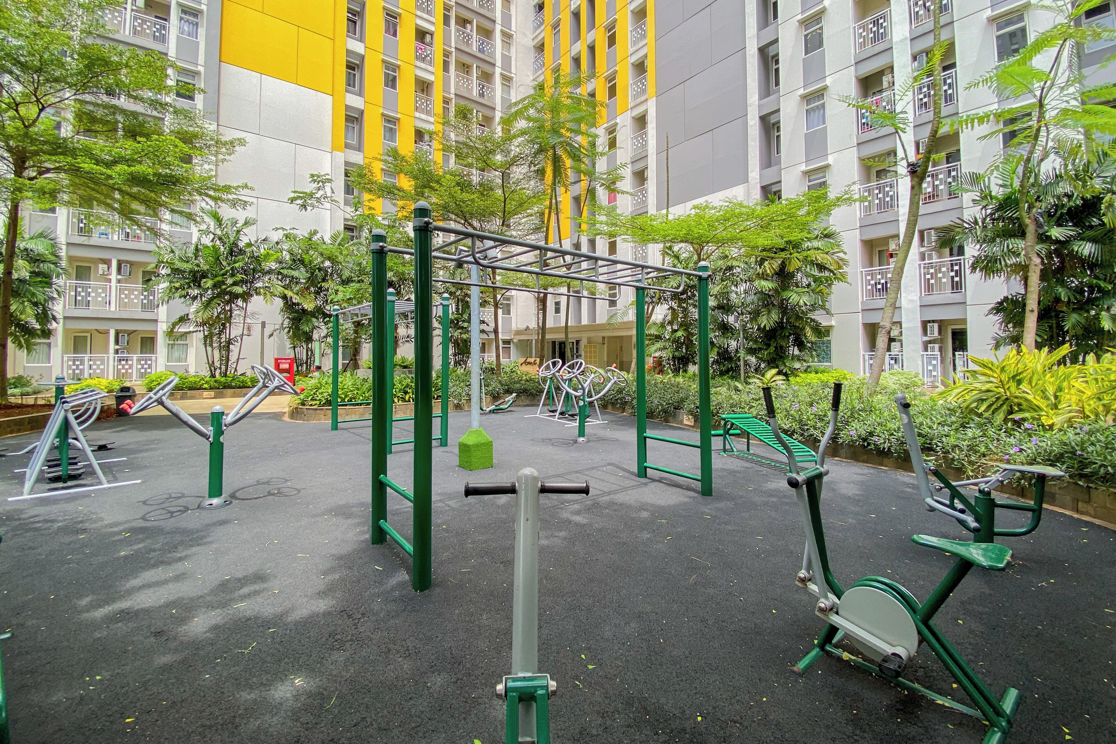 An outdoor gym area with exercise equipment, surrounded by greenery and residential buildings.