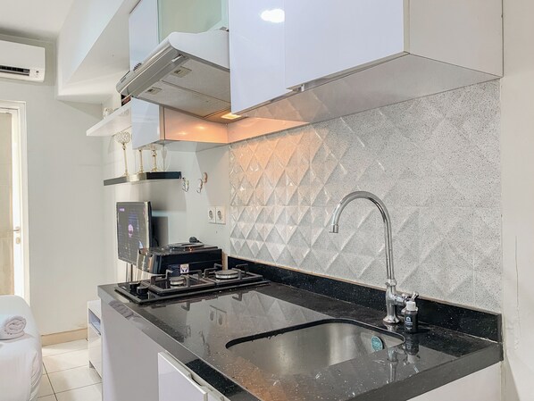 A modern kitchen with a black countertop, stainless steel sink, and a gas stove. - Cozy Living Studio With Direct Access To Pool, Gym And Playground At Springlake Summarecon Bekasi (Bekasi)