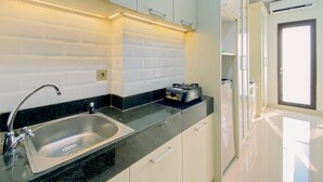 A modern kitchen with a stainless steel sink, white cabinets, and a black countertop. - Good And Homey Studio Apartment At Transpark Cibubur (Depok)