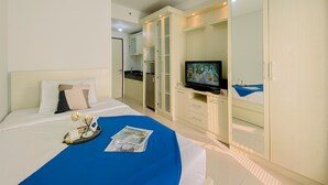 A hotel room with a bed, a television, a wardrobe, and a kitchenette. - Good And Homey Studio Apartment At Transpark Cibubur (Depok)