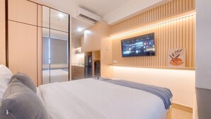 A modern hotel room with a large bed, a flat-screen TV mounted on the wall, and a wooden panel design on the upper wall. - Cozy And Well Furnished Studio Collins Boulevard Apartment (Tangerang)