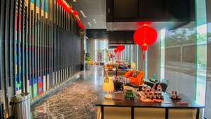 A modern hotel lobby with a long corridor, colorful vertical panels, and a seating area with a table displaying model houses. - Cozy And Well Furnished Studio Collins Boulevard Apartment (Tangerang)