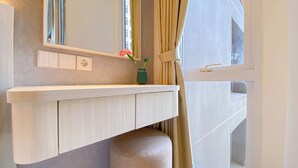 Et badeværelse med et hvidt toiletbord, en grøn vase med blomster og et vindue med gardiner.