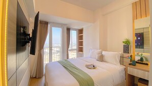 Hotelkamer met een bed, een aan de muur bevestigde televisie, een balkon met gordijnen en uitzicht op de stad.