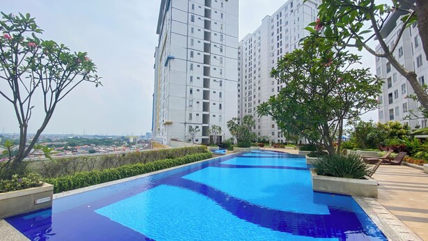 A rooftop swimming pool with clear blue water, surrounded by greenery and tall residential buildings. - Homey And Well Furnished Studio At Bassura City Apartment (Jakarta)