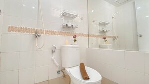 A bathroom with white tiles, a toilet with a towel, a shower, and a mirror. - Homey And Well Furnished Studio At Bassura City Apartment (Jakarta)