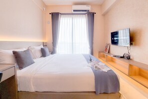 A hotel room with a large bed, a TV mounted on the wall, and a window with curtains. - Cozy Living Studio At Sky House Bsd Apartment (Pagedangan)