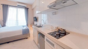 Moderni hotellihuone, jossa on sänky, pieni keittokomero, pesuallas ja ilmastointilaite.