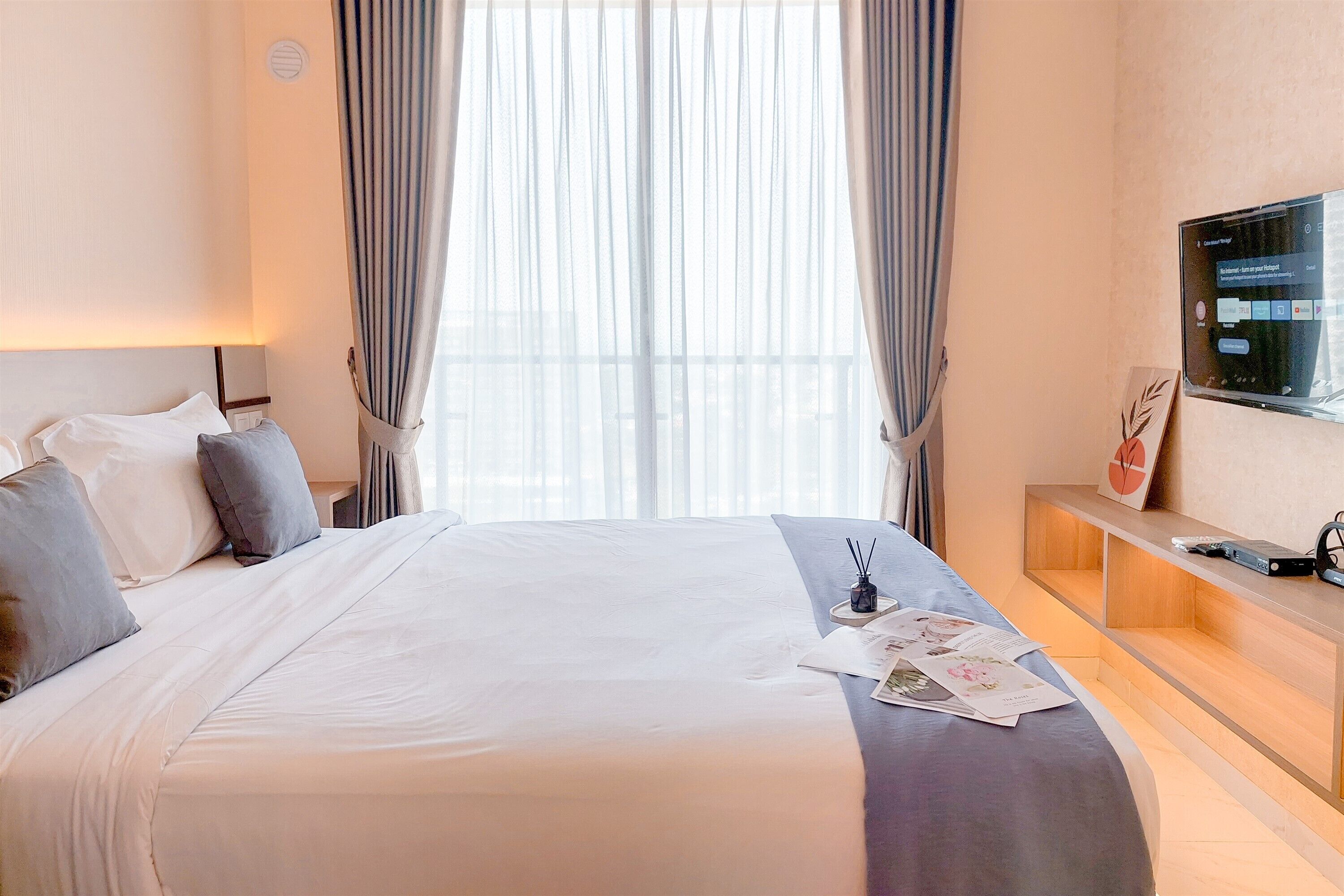 A hotel room with a large bed, a TV on the wall, and a window with curtains.