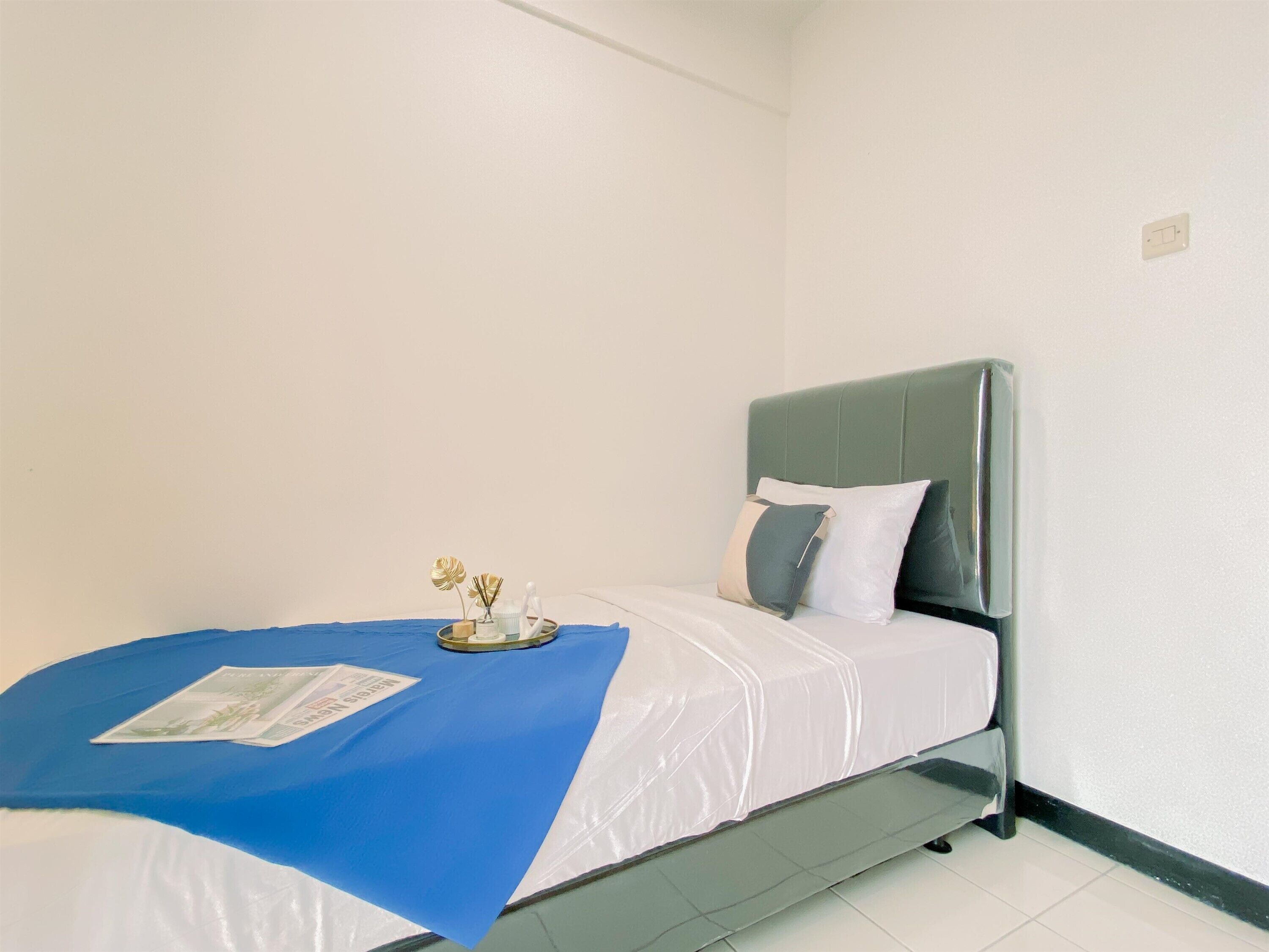 Una cama individual con una colcha azul, una almohada blanca y un florero decorativo con flores.
