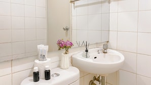 A bathroom with a white sink, a mirror, a towel rack, toiletries, and a vase with flowers. - Good Place And Homey At 2Br Kebagusan City Apartment (Jakarta)