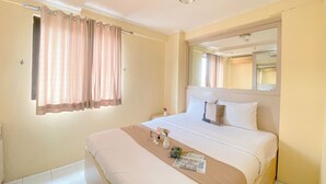 A hotel room with a large bed, a bedside table with a vase of flowers, a window with curtains, and a mirror above the bed. - Good Place And Homey At 2Br Kebagusan City Apartment (Jakarta)