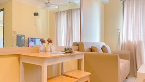 A living room with a beige sofa, wooden coffee table, and two wooden stools. A large water dispenser and a flat-screen TV are visible on the wall. - Good Place And Homey At 2Br Kebagusan City Apartment (Jakarta)