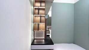 A modern hotel room with a minimalist design, featuring a built-in wooden shelf unit and a small bedside table.