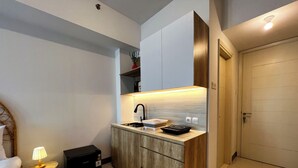 A compact kitchen with a built-in stove, a sink, and a countertop. There is a small table with a lamp next to the bed. - Compact And Best Choice Studio At Anderson Supermall Mansion Apartment (Surabaya)
