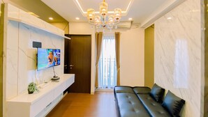 A modern living room with a flat-screen TV, a black leather sofa, a white console table, and a marble wall. - Good And Warm 2Br At Transpark Cibubur Apartment (Depok)