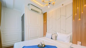 A hotel room with a large bed, a bedside table, an air conditioning unit, and a modern chandelier. - Good And Warm 2Br At Transpark Cibubur Apartment (Depok)