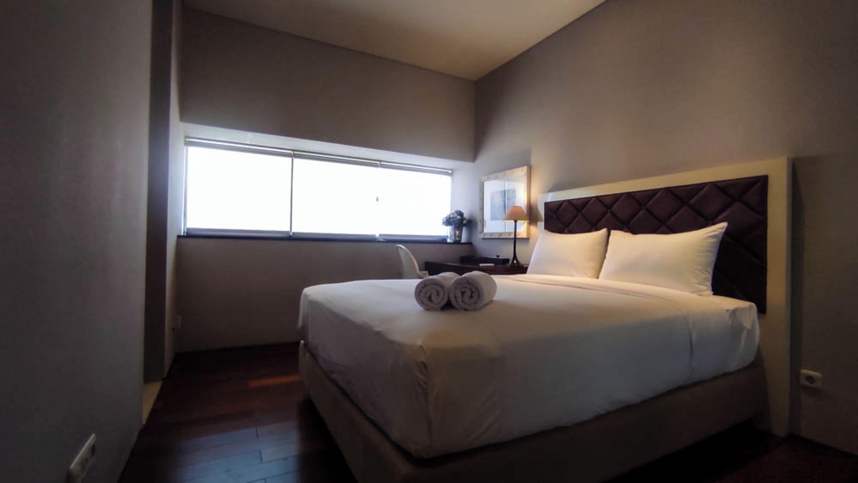 Una habitación de hotel con una cama, un escritorio, una silla, una lámpara y una ventana.