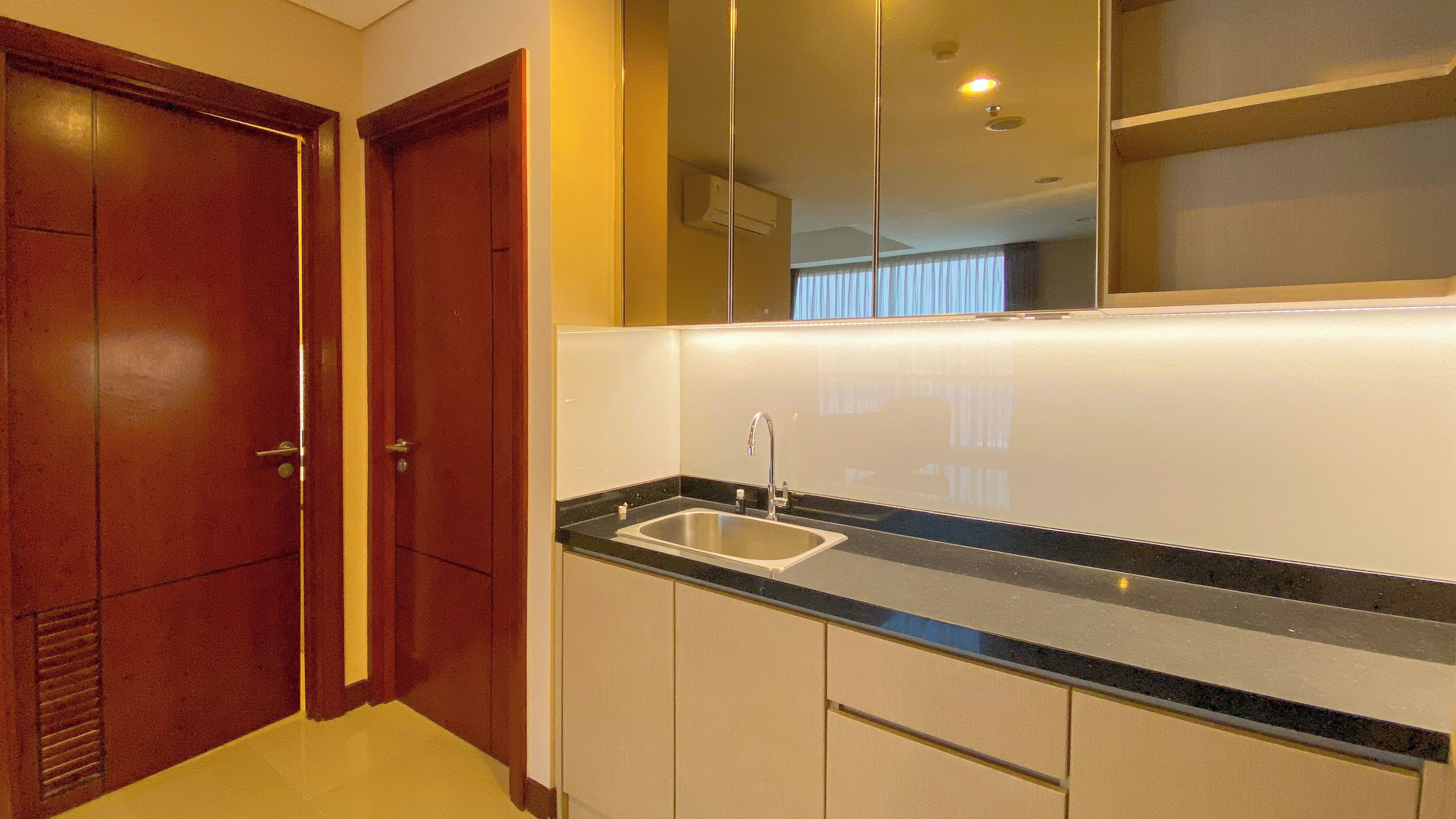 A modern kitchen with a stainless steel sink, wooden cabinets, and a large mirror above the countertop.