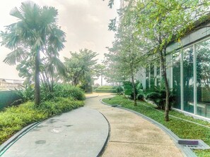 Stroll along the landscaped pathway, lined with lush greenery and palm trees, to the entrance of this building with large windows.