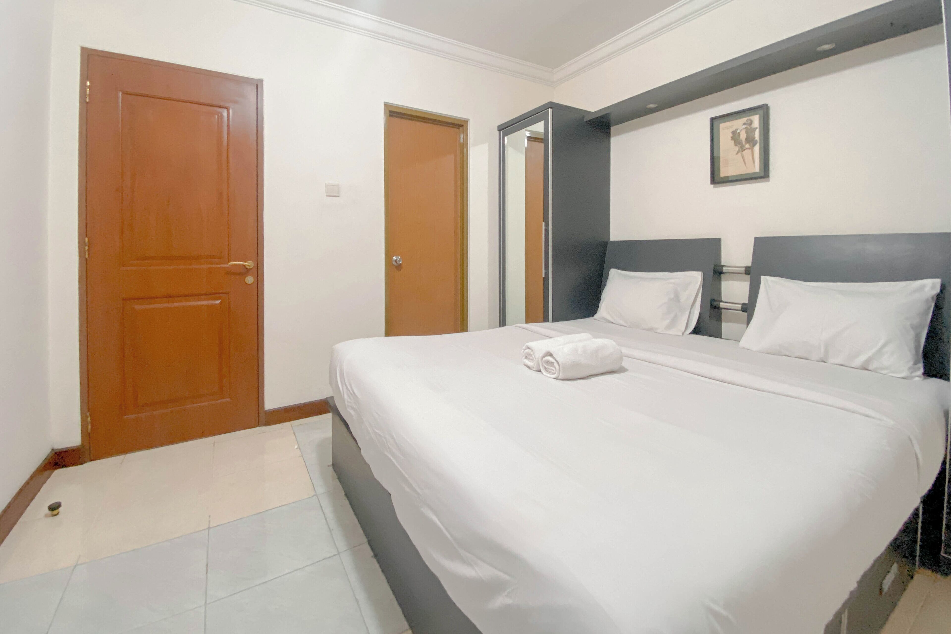 Habitación de hotel con una cama grande, una puerta de madera, un espejo y un cuadro enmarcado en la pared.