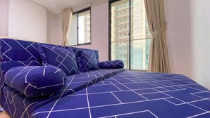 Une chambre moderne avec un grand lit, une literie à motifs géométriques et une vue sur les gratte-ciel par la fenêtre.