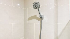 Une douche équipée d’un pommeau de douche à main et d’un flexible, le tout fixé sur un mur carrelé.