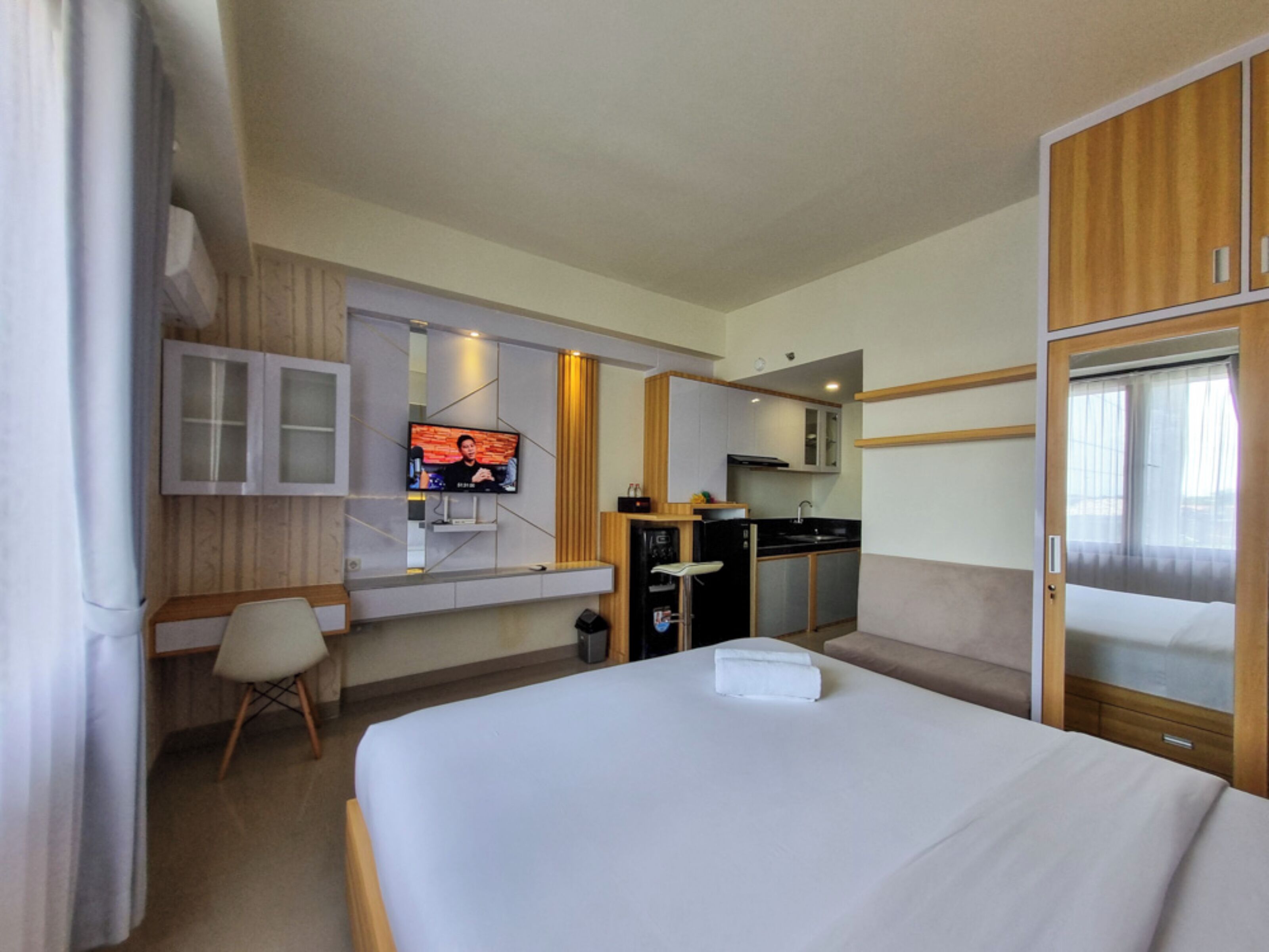 Quarto de hotel com cama, televisão presa à parede, pequena cozinha e guarda-roupa de madeira.