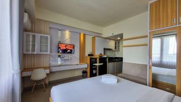 Quarto de hotel com cama, televisão presa à parede, pequena cozinha e guarda-roupa de madeira.