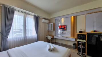 Quarto de hotel com cama, escrivaninha, televisão e minibar.